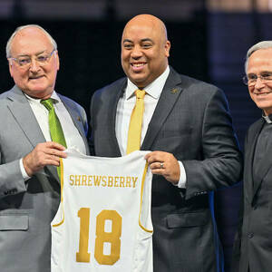 Athletic Director Jack Swarbrick and Rev. John I. Jenkins, C.S.C. stand on either side of incoming Men's Basketball Coach Micah Shrewsberry, who holds a Shrewsberry jersey with the number 18 on it