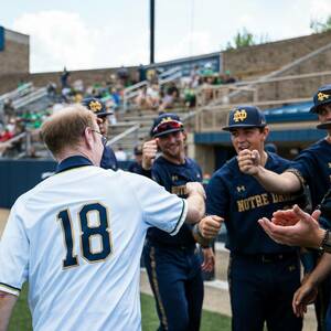 Rev. Robert A.Dowd, C.S.C., wears a baseball jersey with the number 18 and shakes hands with Notre Dame baseball players