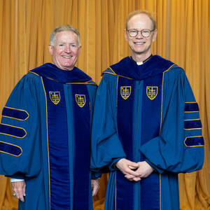 Fr. Bob and John Veihmeyer wear blue regalia and stand in front of gold pipe and drape