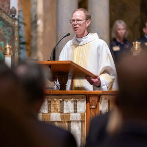 Fr. Robert Dowd stands at a podium, wearing white and gold liturgical robes