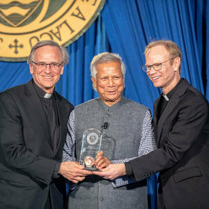 Fr. Jenkins and Fr. Dowd stand on either side of Nobel Laureate Muhammad Yunus. Together they are holding the Ford Family Notre Dame award.